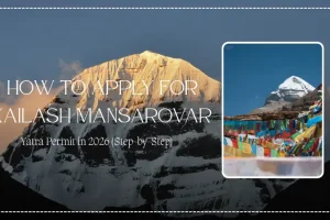 A stunning view of Mount Kailash illuminated by golden sunrise light, showcasing its iconic snow-covered pyramid-shaped summit against a clear Himalayan sky. The image features a smaller inset photograph of Mount Kailash surrounded by colorful Tibetan prayer flags, symbolizing the spiritual significance of the Kailash Mansarovar Yatra. Overlay text reads "How to Apply for Kailash Mansarovar Yatra Permit in 2026 (Step-by-Step)," making this an ideal featured image for a guide on Kailash Mansarovar registration, permit application, pilgrimage planning, and travel requirements for the sacred journey to Mount Kailash and Lake Mansarovar.